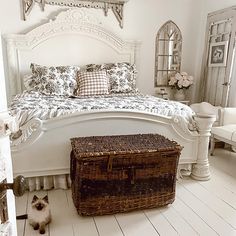 a bedroom with a white bed, basket and cat sitting on the floor next to it