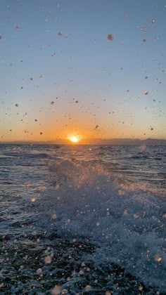 the sun is setting over the ocean with water splashing on it's surface