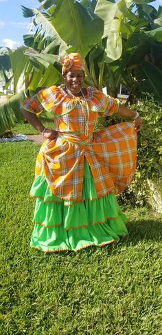 a woman in an orange and green dress is standing on the grass with her arms behind her back