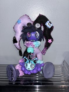 a purple and black stuffed animal sitting on top of a metal shelf next to a white wall