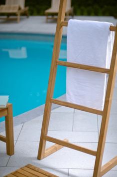 a wooden towel rack next to a swimming pool with towels hanging from it's sides