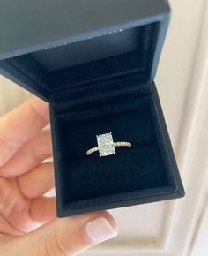 a woman's hand holding an engagement ring in a box