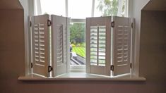 an open window with shutters in front of it and a view of a park