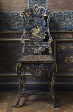 an old wooden chair sitting in front of a wall with ornate designs on the back