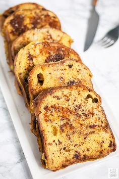 slices of french toast on a white plate with a fork and knife in the background