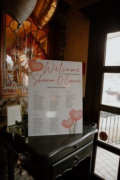 a welcome sign sitting on top of a black table next to a window with balloons