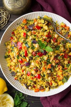 a white bowl filled with rice and vegetables next to lemons on a purple cloth