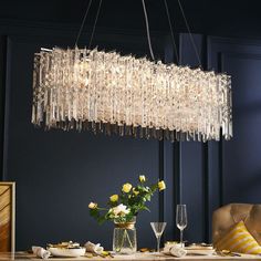 a chandelier hanging over a dining room table with flowers in the vase on it