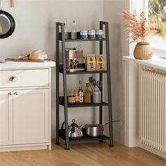 a kitchen with white walls and wooden floors has a black shelving unit in the corner