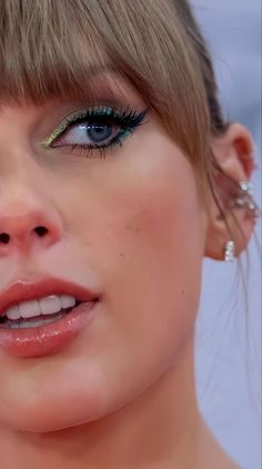 a close up of a woman with blue eyes and green eyelashes wearing gold ear rings