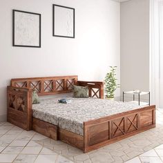 a wooden bed frame with drawers underneath it in a white walled room next to a potted plant and two framed pictures on the wall