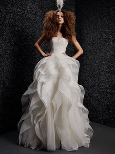 a woman in a white wedding dress with feathers on her head and long curly hair