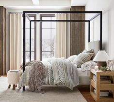 a bedroom with a four poster bed and beige curtains on the window sill, along with a white rug