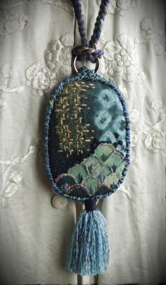 a blue and white necklace hanging from a hook on a lace tablecloth covered curtain