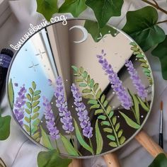 a mirror with purple flowers painted on it next to green leaves and scissors, along with other items