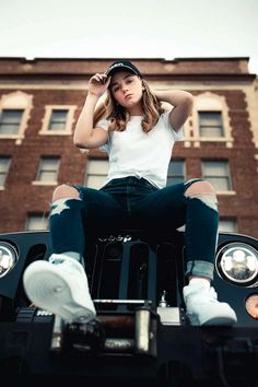 a woman sitting on the back of a car in front of a tall brick building