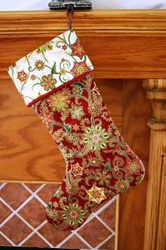 a christmas stocking hanging from a fireplace mantel with red and gold floral designs