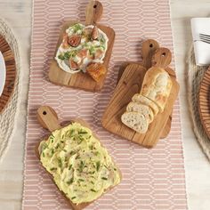 three wooden cutting boards topped with food on top of a pink and white table cloth