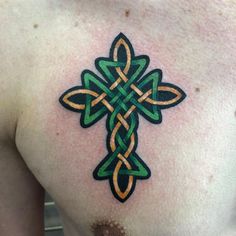 a cross tattoo on the back of a man's left shoulder, with green and orange colors