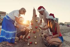 three women are decorating a christmas tree on the beach