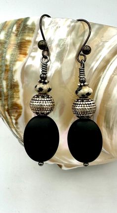 Eye catching long oval onyx earrings with textured round silver tone beads topped with Dalmatian jasper and black vintage ball hooks. The perfect accent piece to your boho style! Artisan Black Jewelry With Ear Wire, Handmade Black Oval Beads Jewelry, Handmade Black Jewelry With Oval Beads, Black Natural Stone Dangle Earrings, Black Natural Stone Oval Beaded Jewelry, Artisan Black Earrings With Round Beads, Black Jewelry With Oval Natural Stones, Artisan Black Oval Beads Jewelry, Artisan Black Oval Bead Jewelry