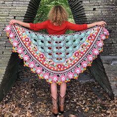 a woman in red shirt holding up a colorful crocheted shawl