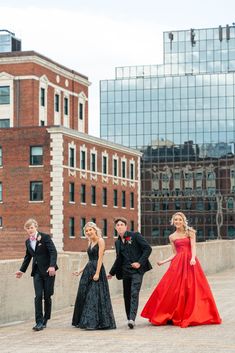 four people dressed in formal wear standing on a bridge with buildings in the back ground