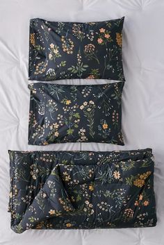 two pillows and one pillow case are laying on a white bed sheet with floral print