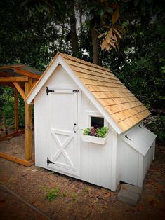 a small white shed with a brown roof and flower box on the window sill