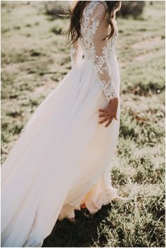 a woman in a long white dress is walking through the grass with her hands on her hips