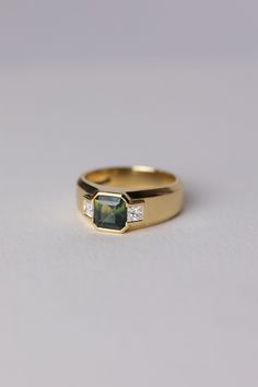 a yellow gold ring with an emerald stone and two diamonds on the side, sitting on a white surface