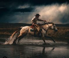 a man riding on the back of a white horse across a river under a cloudy sky