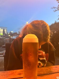 a woman sitting at a table with a beer in front of her and the sun behind her