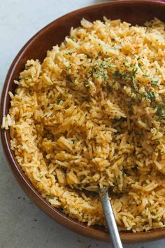 a brown bowl filled with rice and garnished with parsley next to a spoon