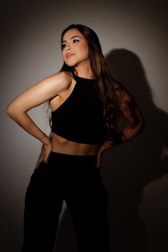 a beautiful young woman posing for the camera in black pants and cropped tank top