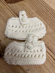 two white crocheted baby booties sitting on top of a wooden floor next to each other