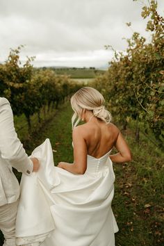 a bride and groom walking through an apple orchard in their wedding attire, back to the camera