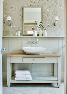 a white sink sitting under a bathroom mirror next to a wooden table with towels on it