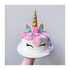 a cake decorated with flowers and a unicorn's head is being held by a hand