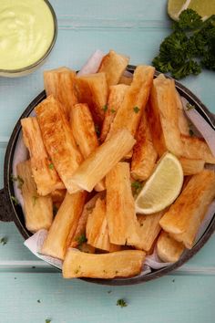 a bowl filled with fried food next to a cup of sauce and lemon wedges