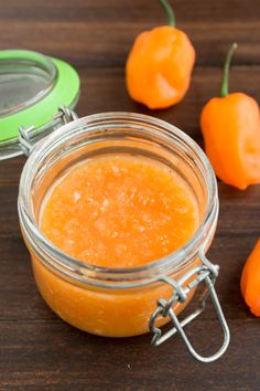 a glass jar filled with orange colored liquid next to some peppers on a wooden table