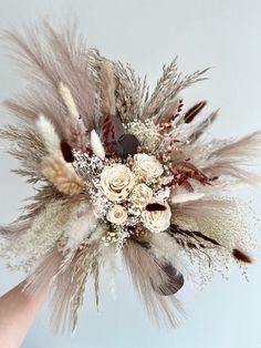 a bouquet with feathers and flowers in it is being held by someone's hand