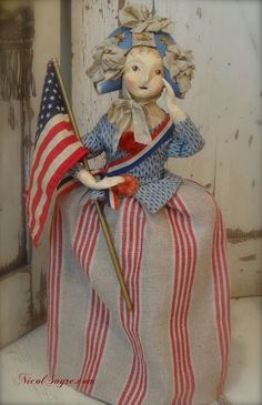 a small doll sitting on top of a table with an american flag in front of it