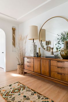 a living room with a large mirror on the wall next to a dresser and lamp