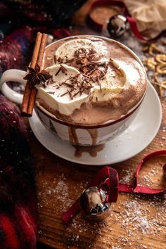 a cup of hot chocolate with whipped cream and cinnamon on the side, surrounded by christmas decorations