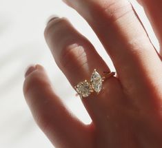 a person's hand holding a ring with two diamonds on it and the middle finger