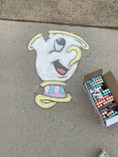 a box of crayons sitting on the sidewalk next to a drawing of a cartoon character