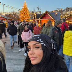 a woman wearing a bandana standing in front of a christmas tree with lights on it