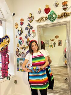 a woman standing in front of a mirror holding an apron over her shoulder and looking at the camera