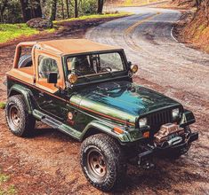 a green jeep with an orange top parked on the side of a dirt road in front of trees